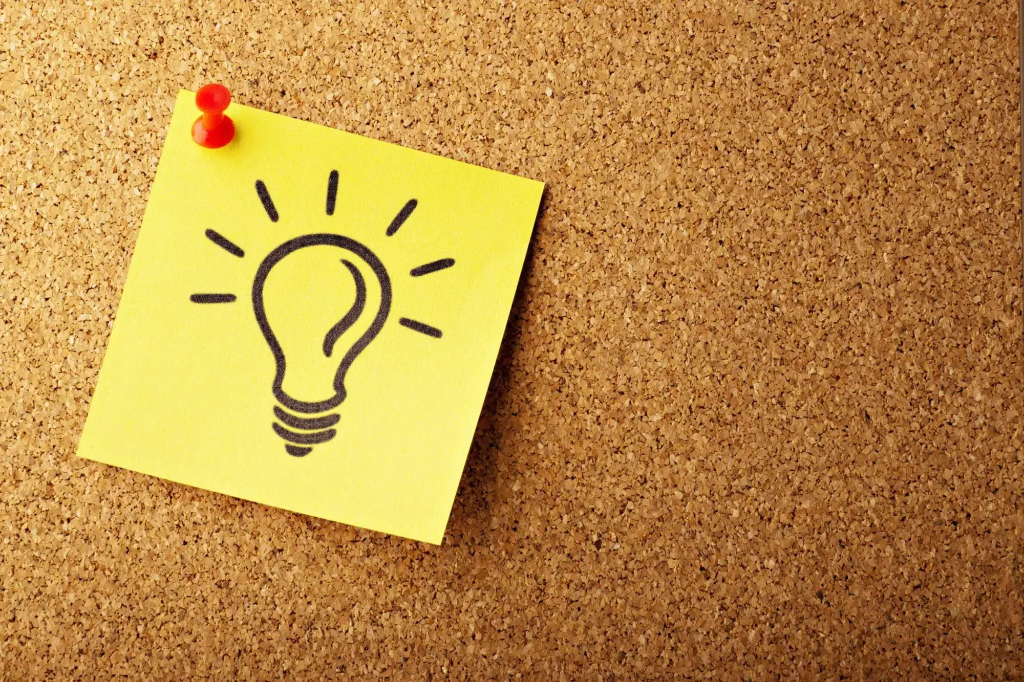 corkboard with a sticky note on it with a shining lightbulb drawn in sharpie